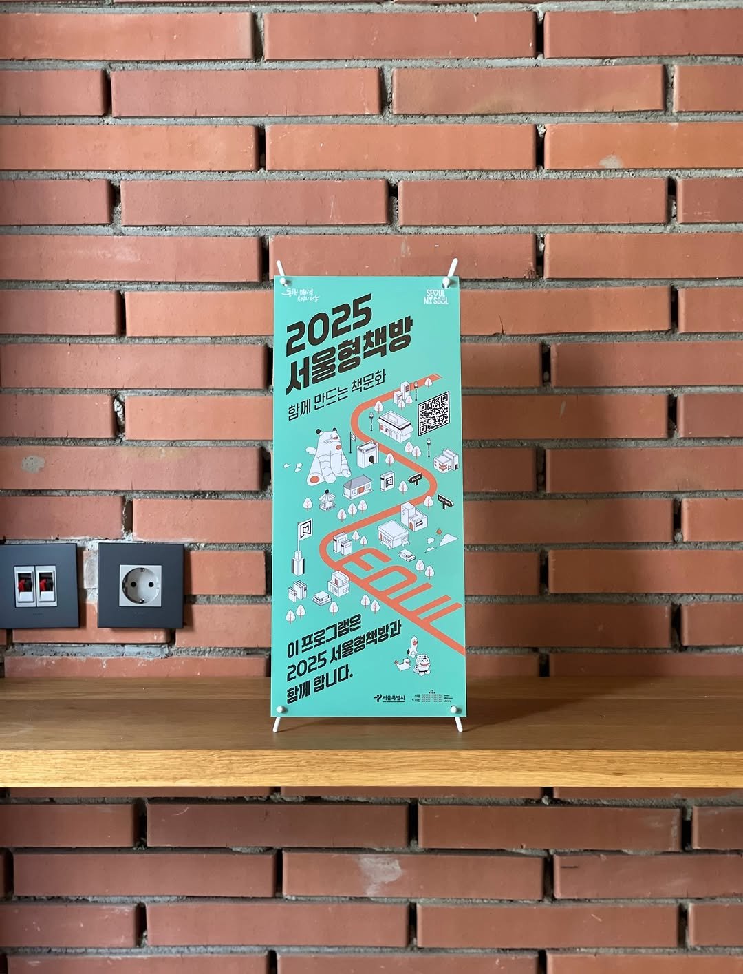 Photo shared by 인공위성 on August 08, 2025 tagging @seoulbookshops. May be an image of matchbook, poster, book, magazine, brick wall and text.