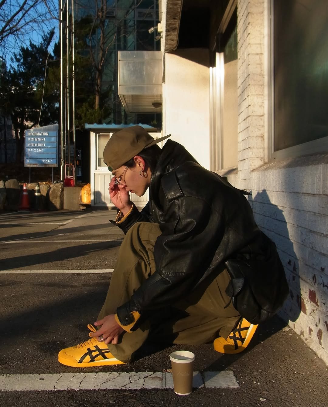 Photo shared by 조우진 on January 15, 2026 tagging @onitsukatigerkr. May be an image of smoking, cigarette, parka, street, curb and text.