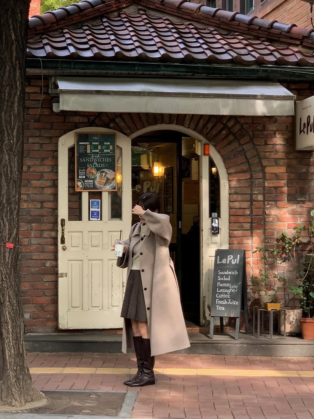 Photo shared by 알로하 on October 30, 2025 tagging @mulette.official. May be an image of duffle coat, overcoat, cornflower, street, brick wall, door and text.