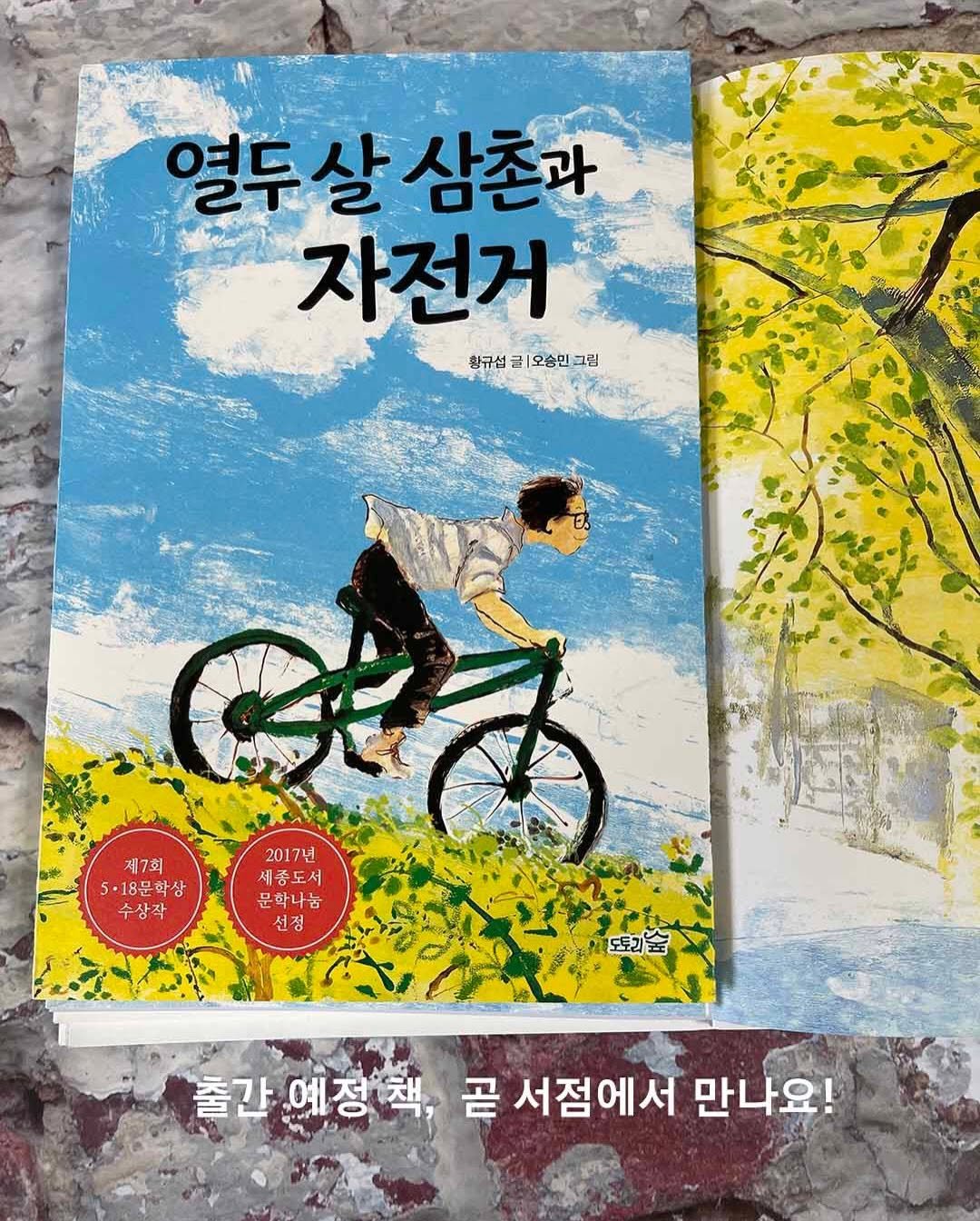 Photo by 도서출판 도토리숲+책숲 on April 14, 2026. May be an image of bicycle, poster, tire, book and text that says '열두살삼촌과 살 삼촌과 열두살 자전거 황규섭 오습민 황구섭글오승민그림 그림 2017년 水家 201 년 제7회 5·18문학상 세종도서 분학나눔 수상작 선점 선정 N·도토리 도토리표 출간예정책 출간예장책,공서점어 출간! 곧 서점에서 만나요!'.