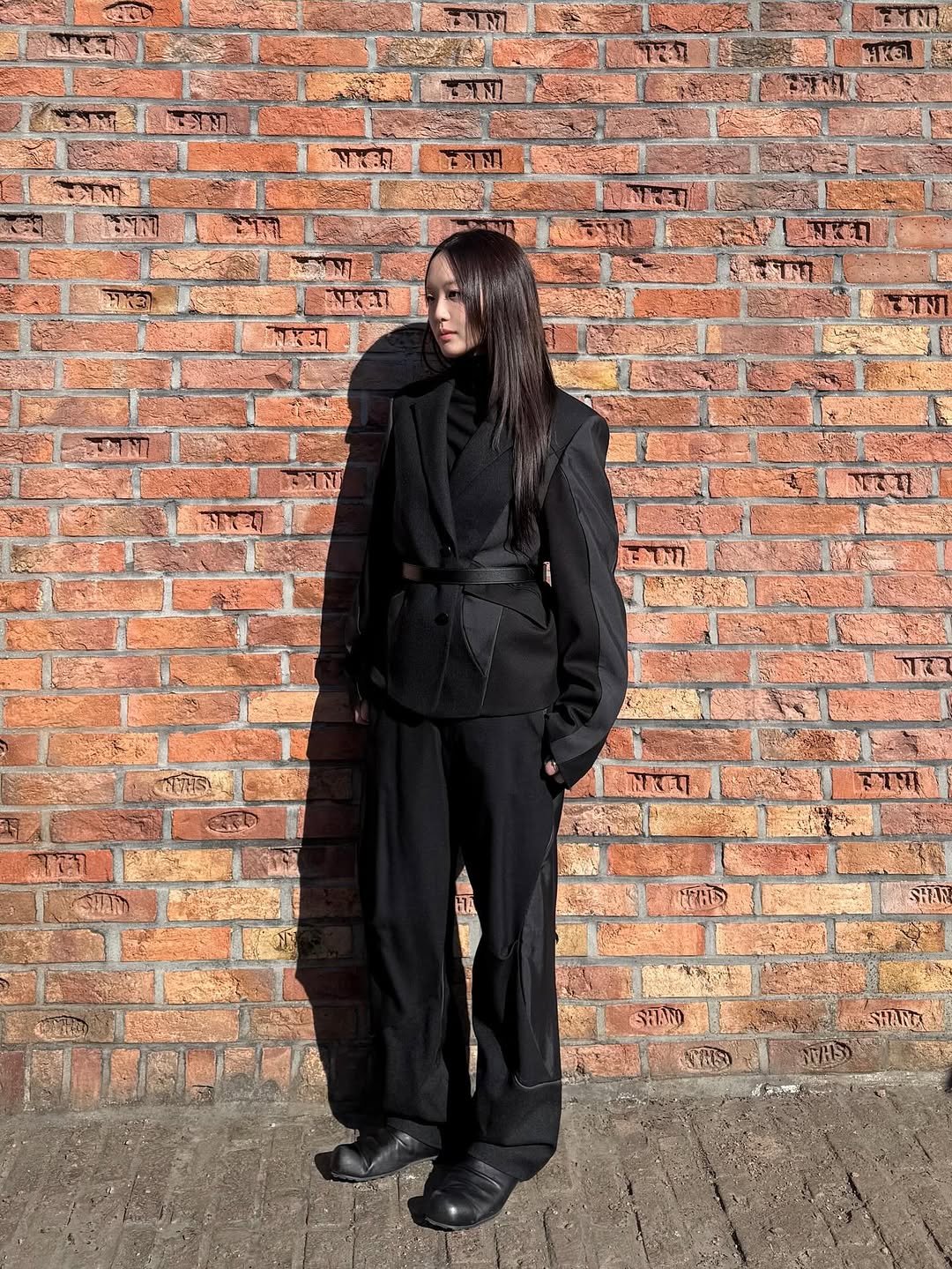 Photo by ADERERROR SPACE on January 23, 2026. May be an image of overcoat, suit, cloak, brick wall and text.