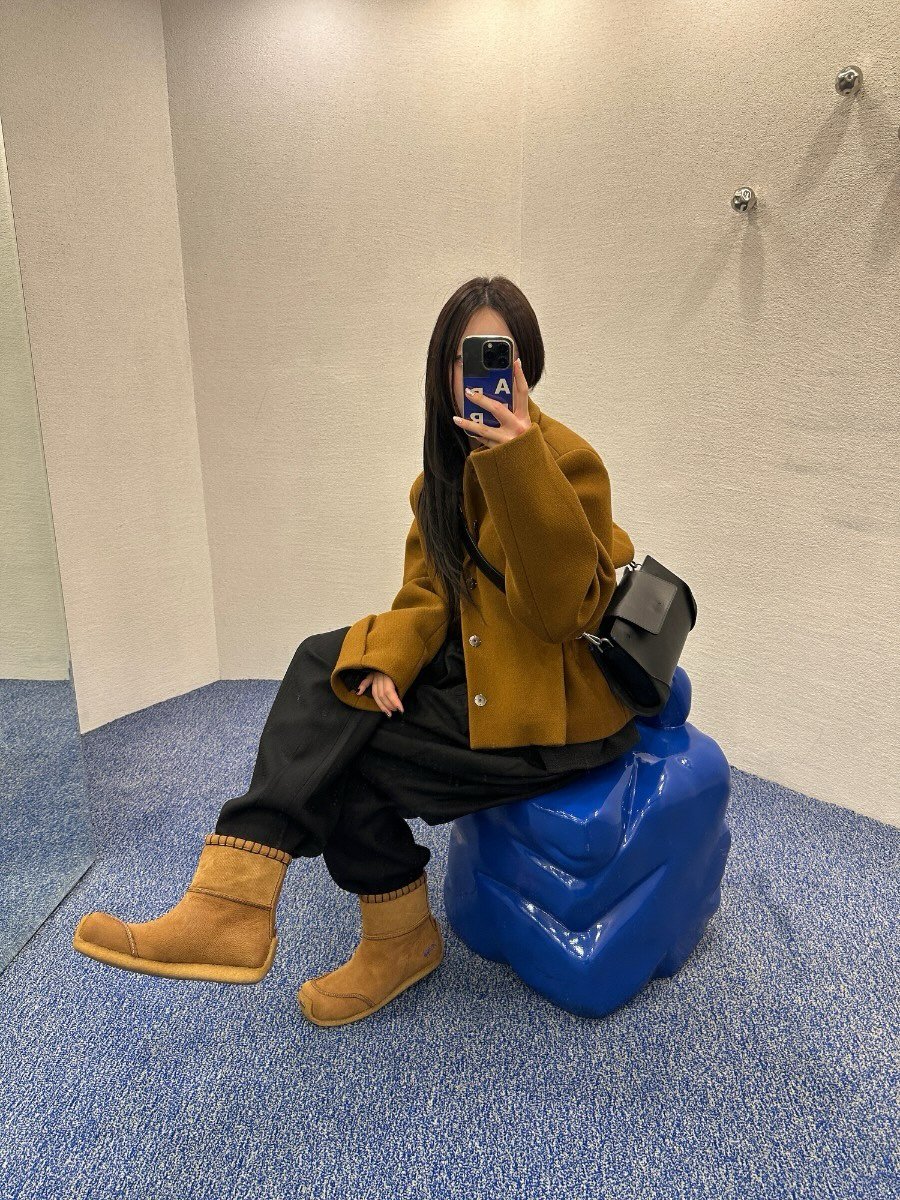 Photo by ADERERROR SPACE on December 30, 2025. May be an image of duffle coat, overcoat, phone, wingtip shoes, boots, parka, mirror, fleece and text.
