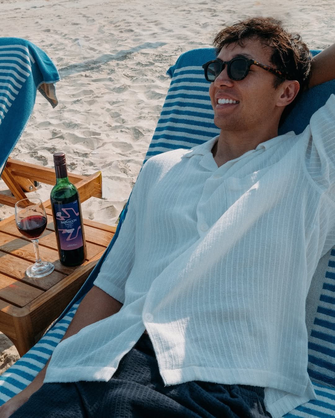 Photo shared by Alex Albon on December 10, 2025 tagging @monsoonvalleyuk, and @monsoonvalley_vineyard. May be an image of towel, wine, deck chair, bath robe, beach and text.