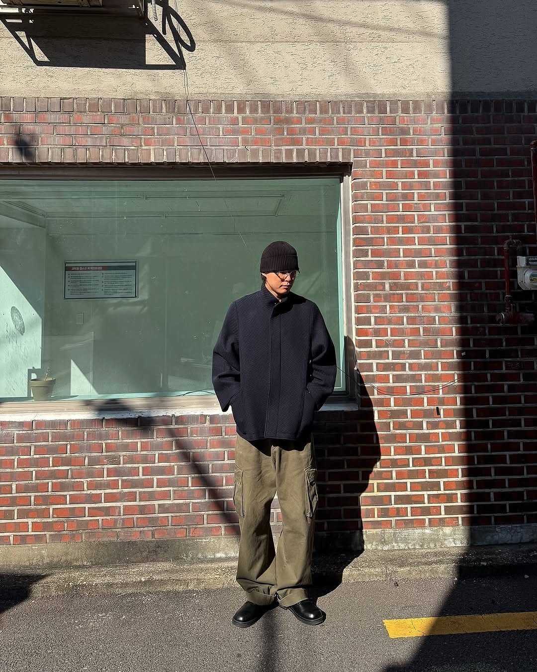 Photo by AMOUPRE 아모프레 on November 21, 2025. May be an image of standing, duffle coat, parka, brick wall and text.