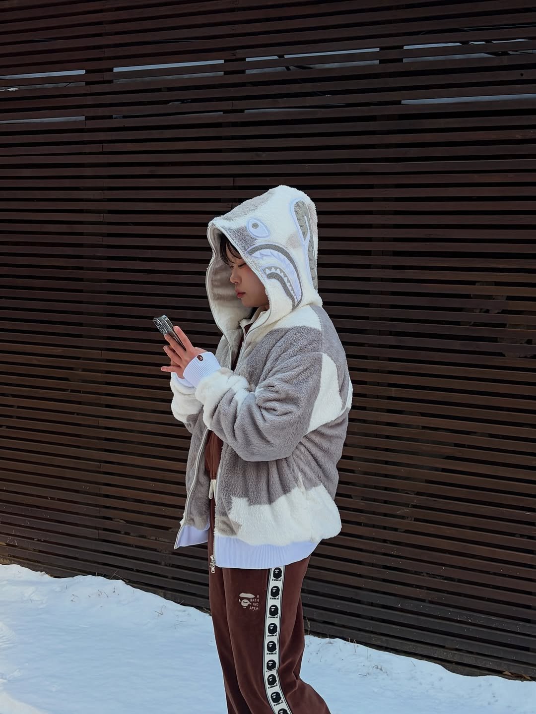 Photo shared by BAPE SEOUL on February 02, 2026 tagging @bapestorekorea, and @bape_seoul. May be an image of standing, duffle coat, phone, fleece, sweatpants, sweatshirt, parka, sweatsuit, snowsuit, jacket, snow and text.