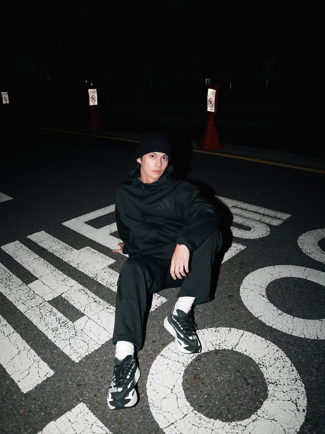 Photo shared by BRIGHT on October 28, 2025 tagging @adidas, and @adidasthailand. May be an image of duffle coat, sweatpants, parka, face mask, road, street, curb and text.