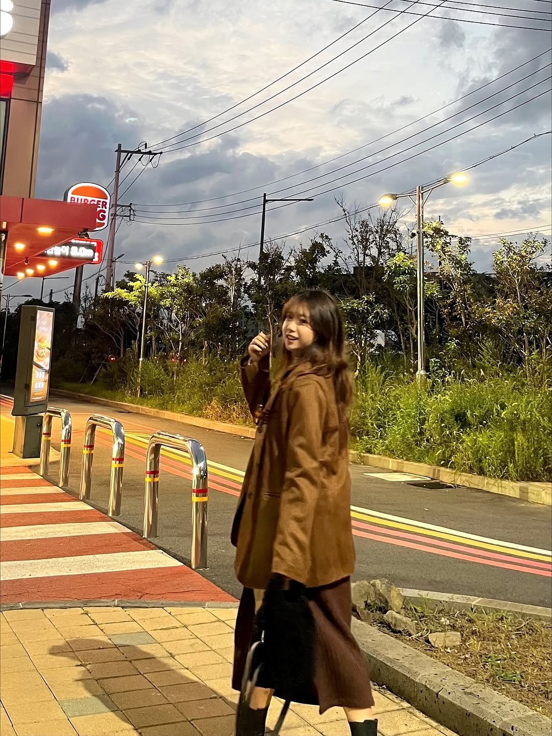 Photo by 송별아 • Byulla on October 28, 2025. May be an image of one or more people, overcoat, duffle coat, parka, street, cloud, road, lamppost and text.