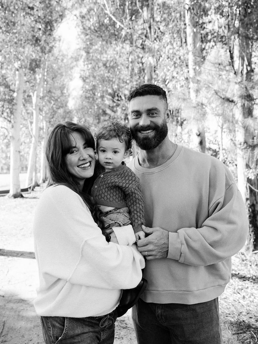 Photo shared by Chris Bumstead on November 27, 2025 tagging @courtneykiing, and @karlykreative. May be a black-and-white image of one or more people, baby, beard, people smiling, tree, park and text.