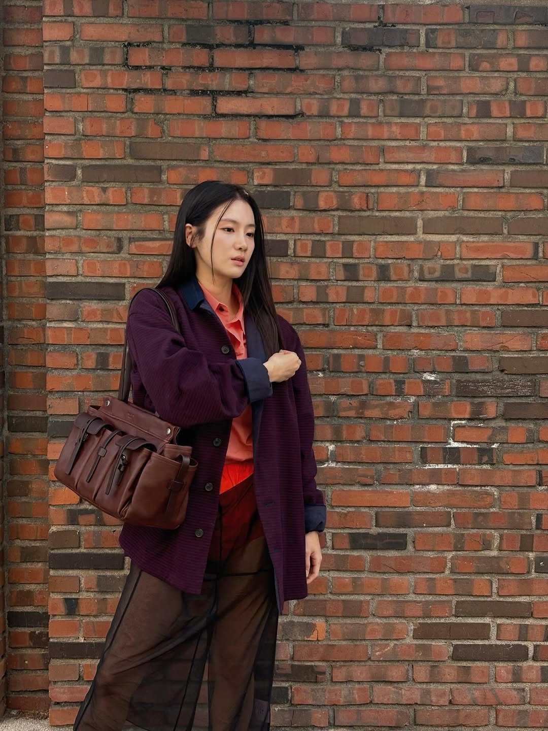 Photo shared by 박주현 on March 26, 2026 tagging @prada. May be an image of duffle coat, overcoat, brick wall and text.