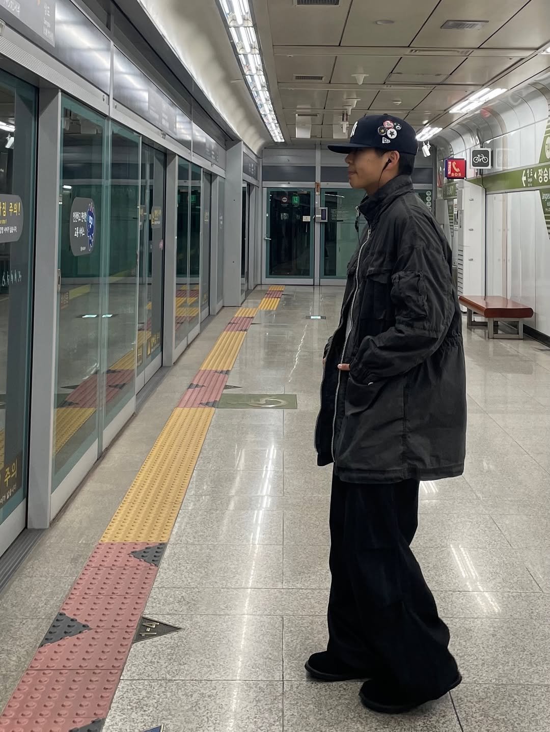 Photo shared by 정인 on December 24, 2025 tagging @newerakorea, @areuban_official, and @999humanity. May be an image of one or more people, people standing, overcoat, duffle coat, turnstile, hat, parka, street, terminal and text that says '즈의 መራ! 御號 半 G+C'.