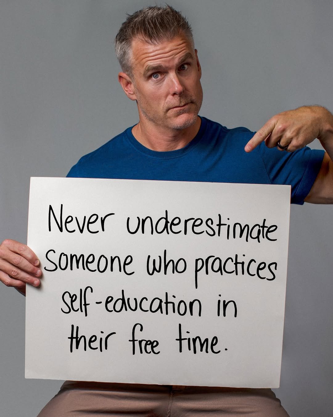 Man holding a sign that reads 'Never underestimate someone who practices self-education in their free time.'