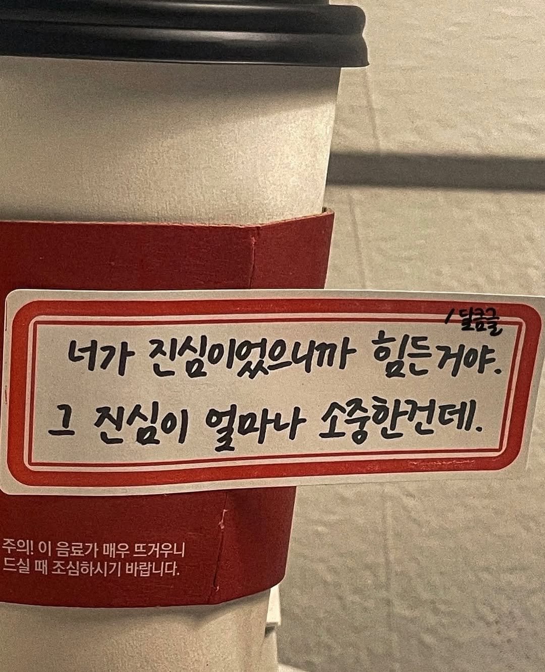 Photo by 달큼글, 예원 on December 11, 2025. May be an image of coffee cup and text that says '너가 진심이었으니까 힘든거야. 그 진심이 얼마나 소중한건데. 주의! 이 음료가 매우 뜨거우니 드실 때 조심하시기 바랍니다.'.