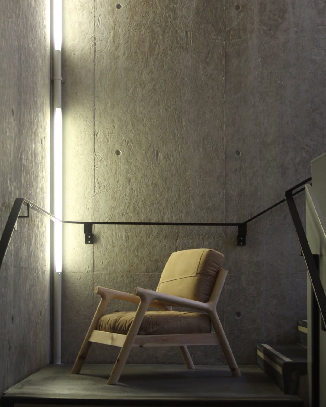 A handmade wooden chair sits at the foot of a stairwell.