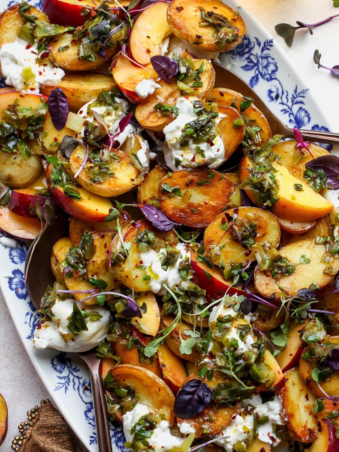 Crispy potato and peach salad with burrata and charred scallion dressing styled on a blue and white platter.