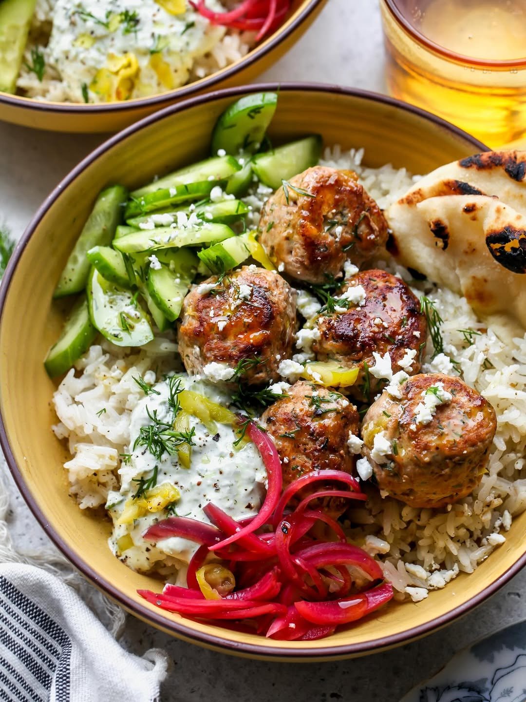 Pepperoncini feta turkey meatballs styled in a yellow bowl with white rice, cucumbers, tzatziki, and pickled red onions.
