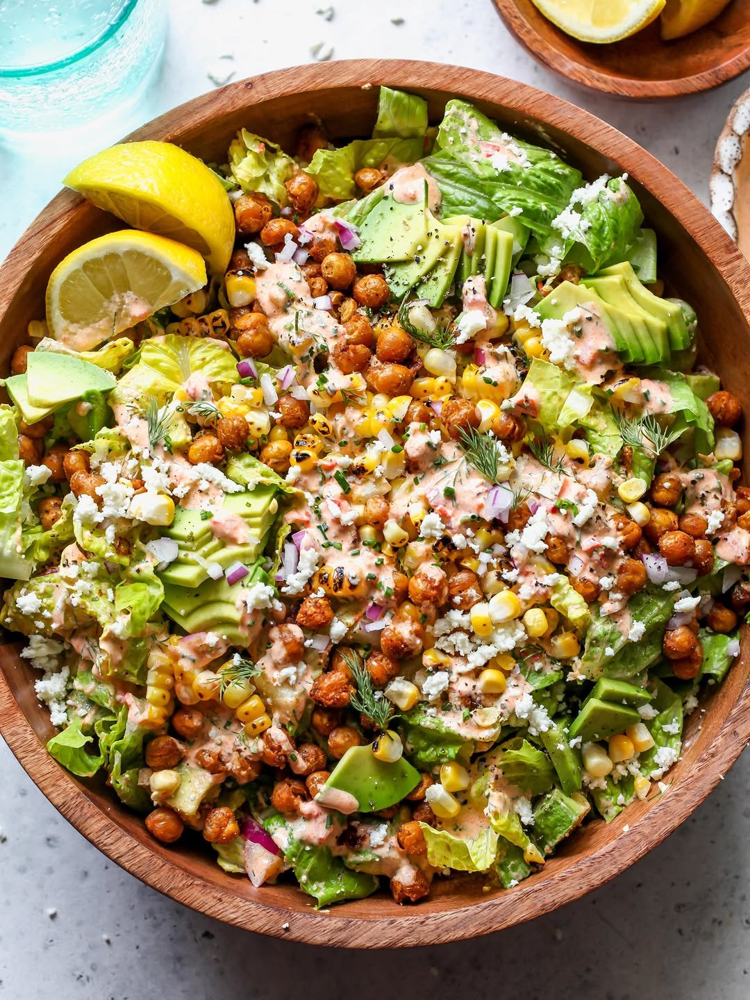 Crispy chickpeas, grilled corn, and romaine salad topped with harissa ranch dressing, styled in a wooden serving bowl.