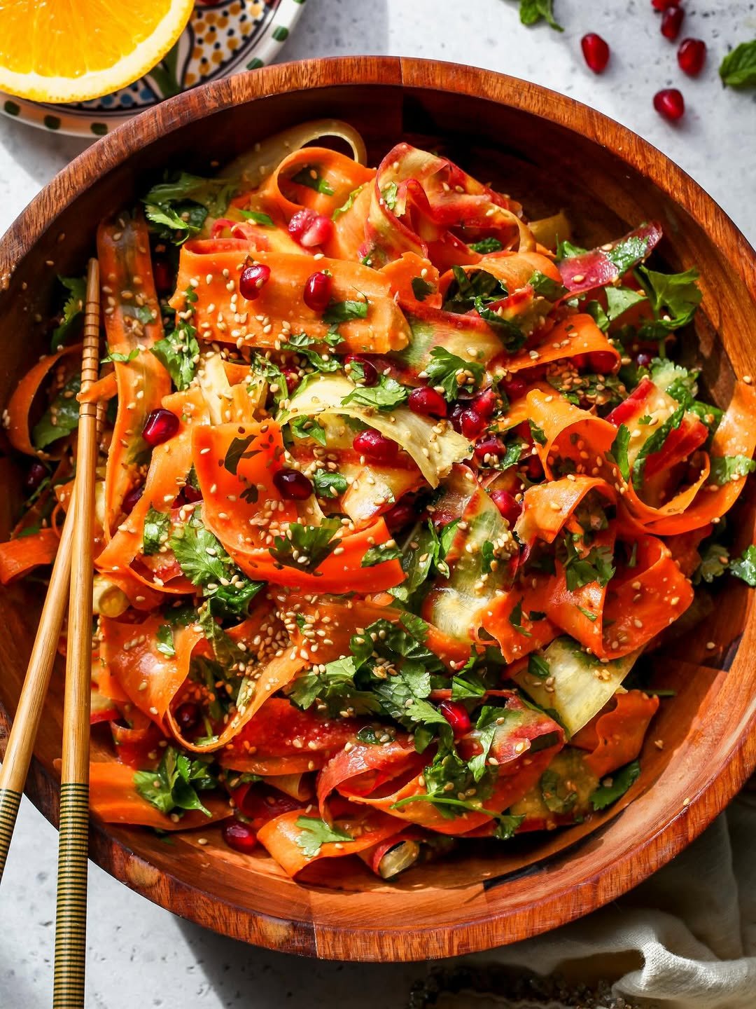 Shaved carrot salad with miso ginger dressing, styled in a large wooden serving bowl with chopsticks resting on the left-hand side.