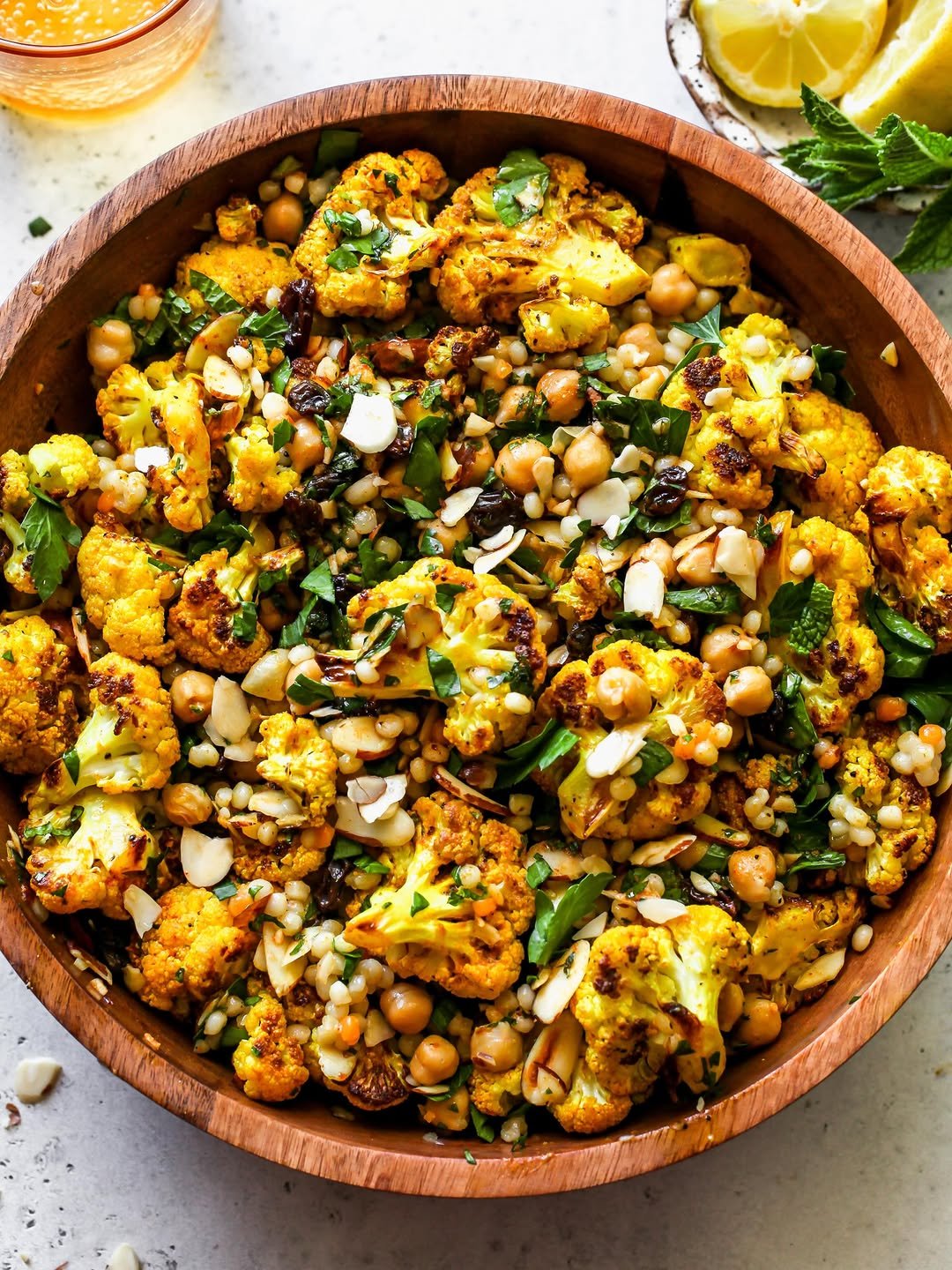 Moroccan cauliflower and pearl couscous salad styled in a wooden serving bowl topped with almonds, parsley, and dressing.