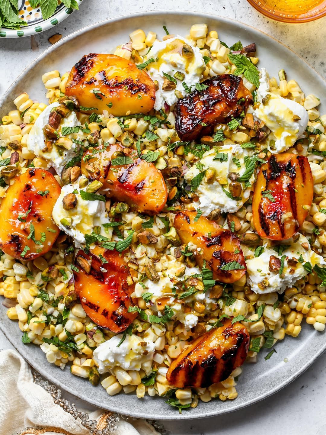Grilled peach and corn salad styled on a serving platter with dollop of burrata cheese and hot honey dressing.