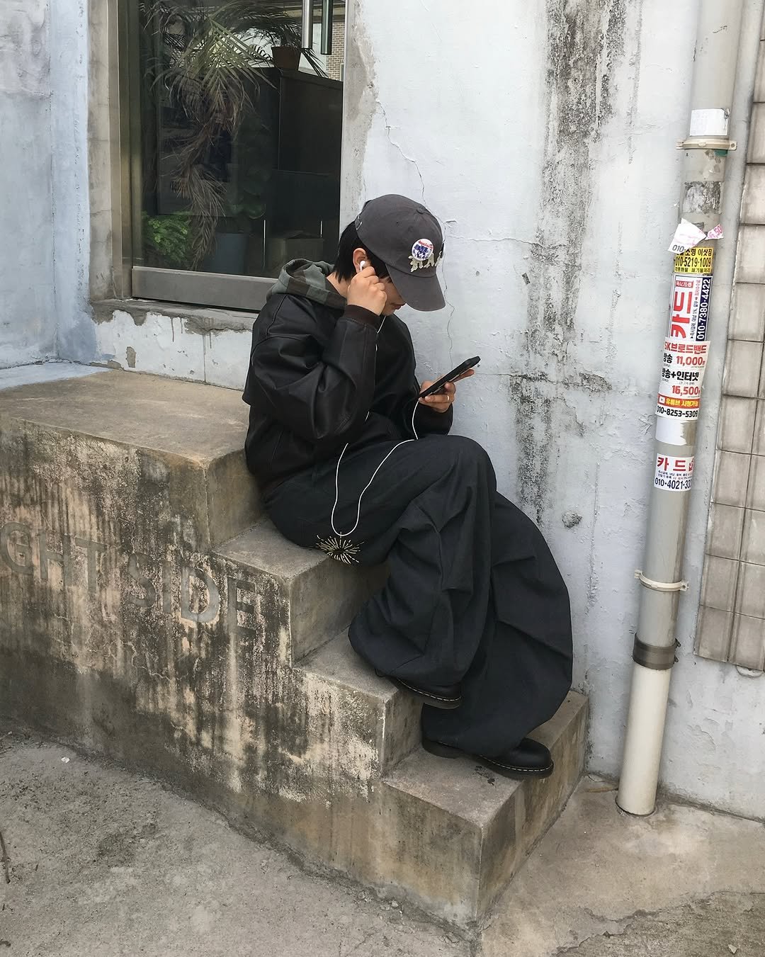Photo shared by 투븐 / TOVN on November 05, 2025 tagging @tovn_official. May be an image of smoking, duffle coat, overcoat, phone, parka, face mask, cigarette, street, curb and text.