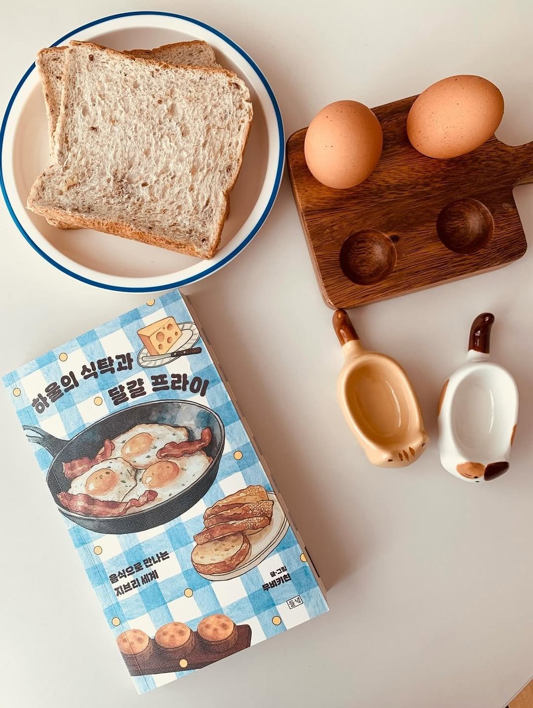 Photo by 도서출판 들녘 on February 09, 2026. May be an image of rye bread, wooden spoon, potholder, placemat, measuring cups, boiled egg, toast, spatula, scrambled eggs and text that says '하울의식탁과 의식탁과 ㅇ달칼프라이 달칼 프라이 만나는 지브리 음식으로 지브리계 離常 황·그림 神・山場 学出 환점)'.
