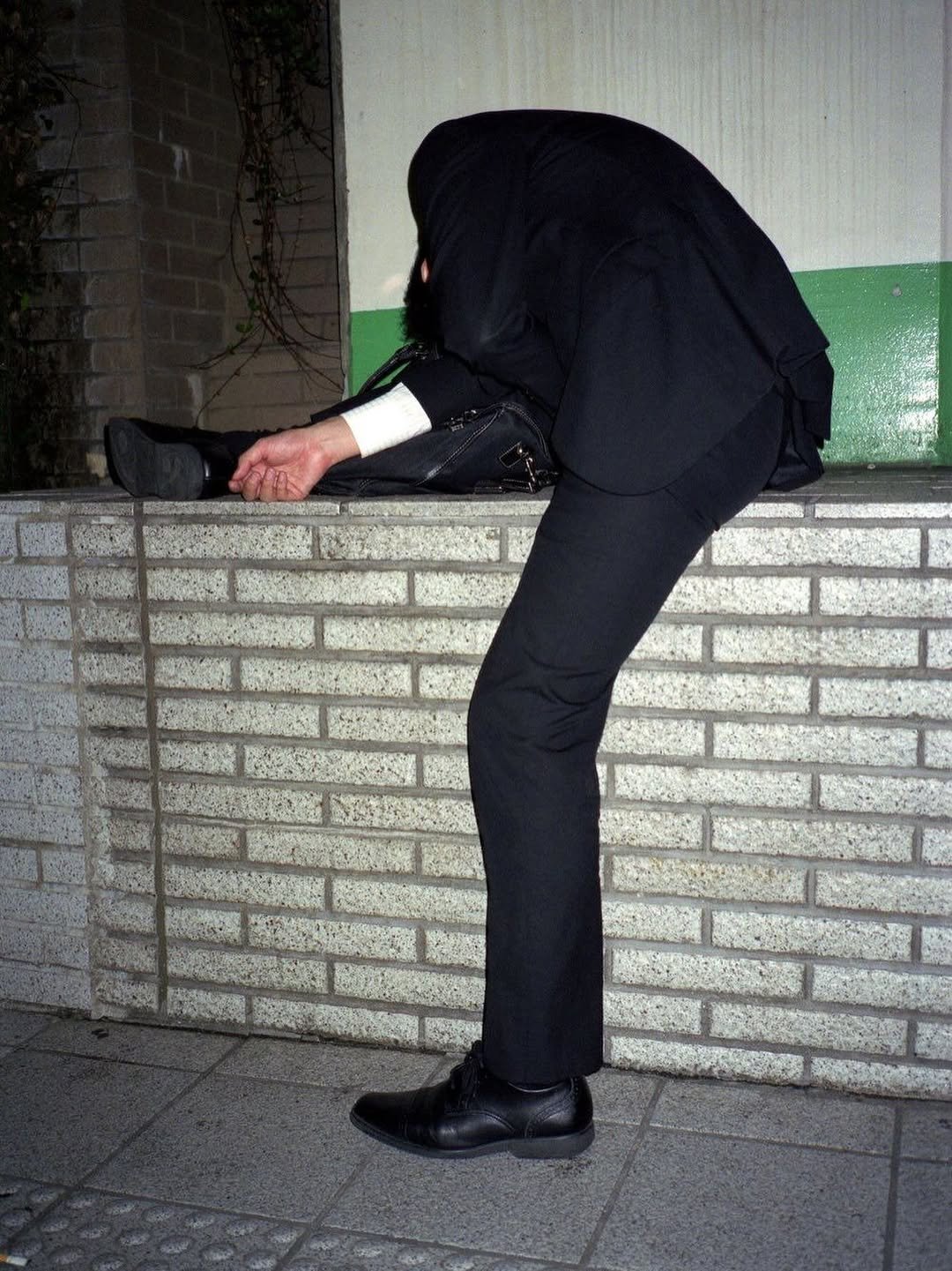 Photo by Echo in Eco on October 09, 2025. May be an image of smoking, wingtip shoes, overcoat, cigarette, manhole, suit, toecap shoes, street, curb and text.