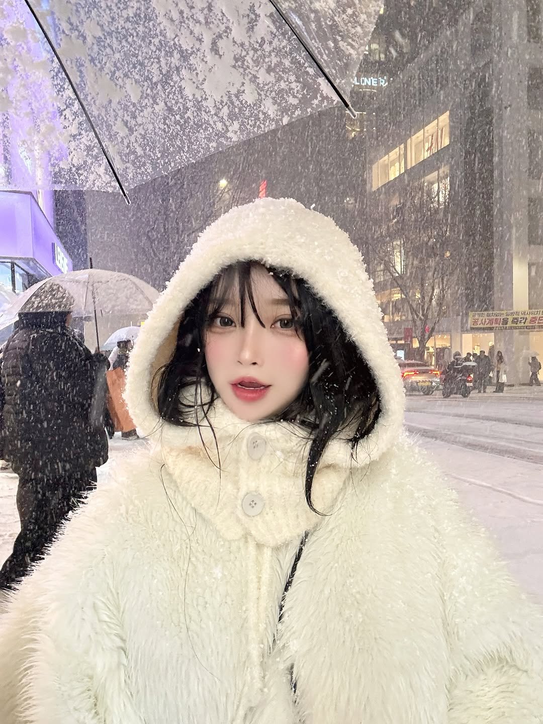 Photo by 오 지은 on December 04, 2025. May be an image of duffle coat, overcoat, goosedown coat, fur coat, raincoat, parka, umbrella, jacket, snow and text.