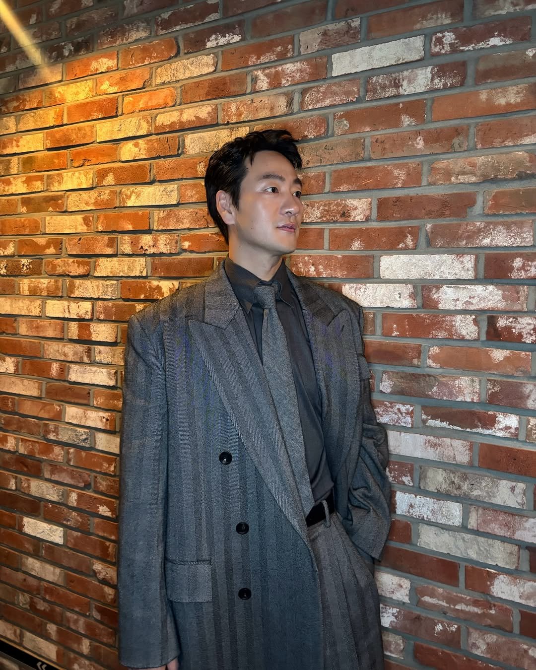 Photo by 박해수 PARKHAESOO on December 03, 2025. May be an image of duffle coat, overcoat, suit, blazer, brick wall and text.