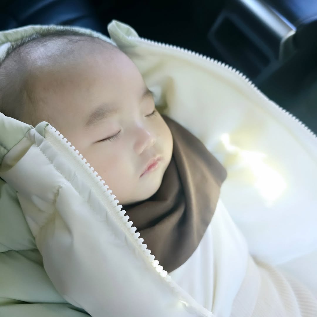 Photo by 한콩이 ☘️ on February 20, 2025. May be an image of 1 person, baby, sleeping, duffle coat, seatbelt, baby bed, sling, parka and text.