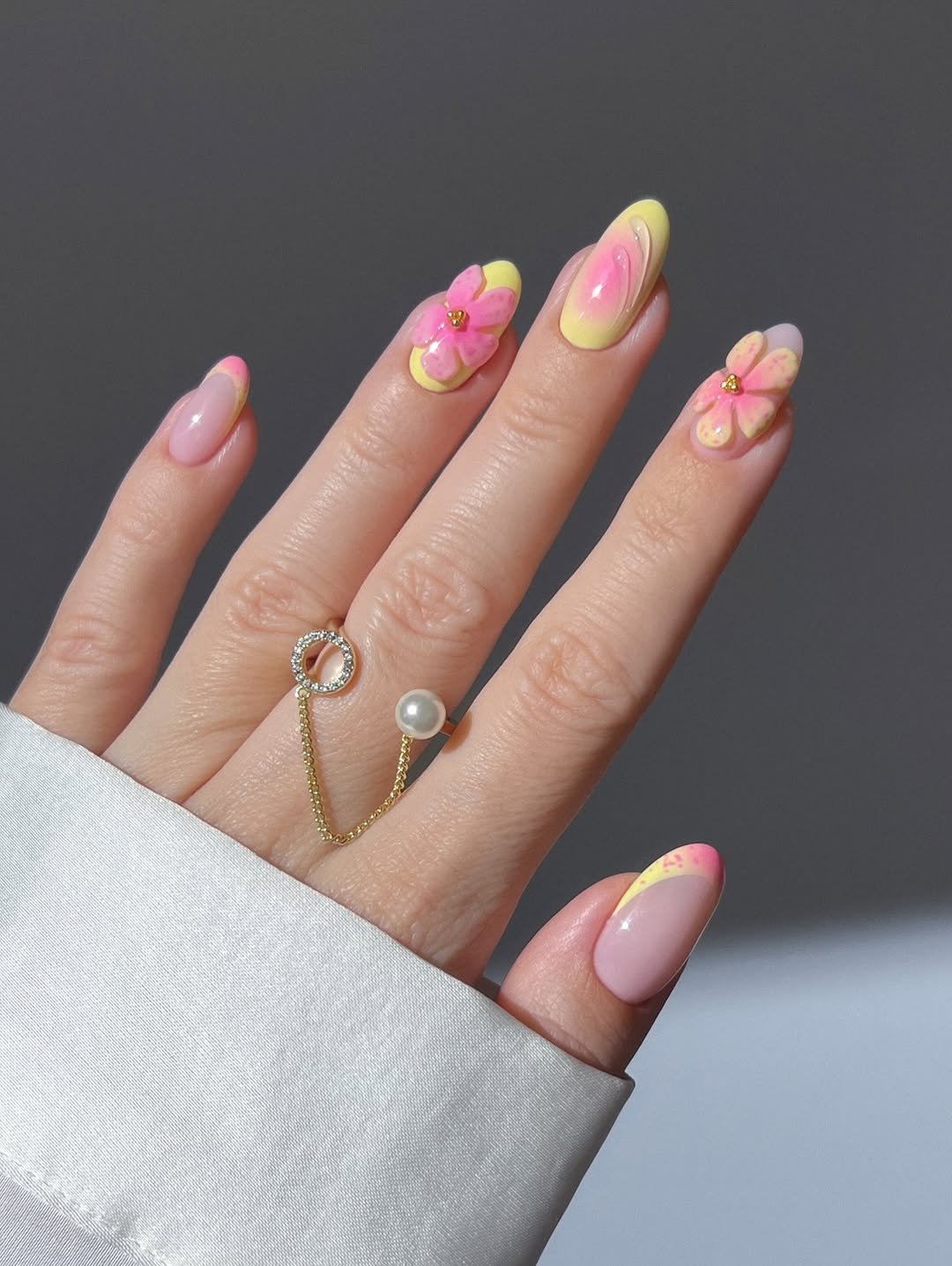 Pastel pink and yellow aura nails, 3D flower nails, spring nails, summer nails, cute nails, french tip nails, almond nails, gold pearl ring with dangling chain, pink nude nails with gold shimmer, gold chrome flower nails, glassy cat eye nails, gold open leaf ring with gems, dainty gold dotted ring, sparkly gold velvet nails, wildflower nails, colorful dainty floral nails, nail stickers, dainty multi cut diamond rainbow ring,