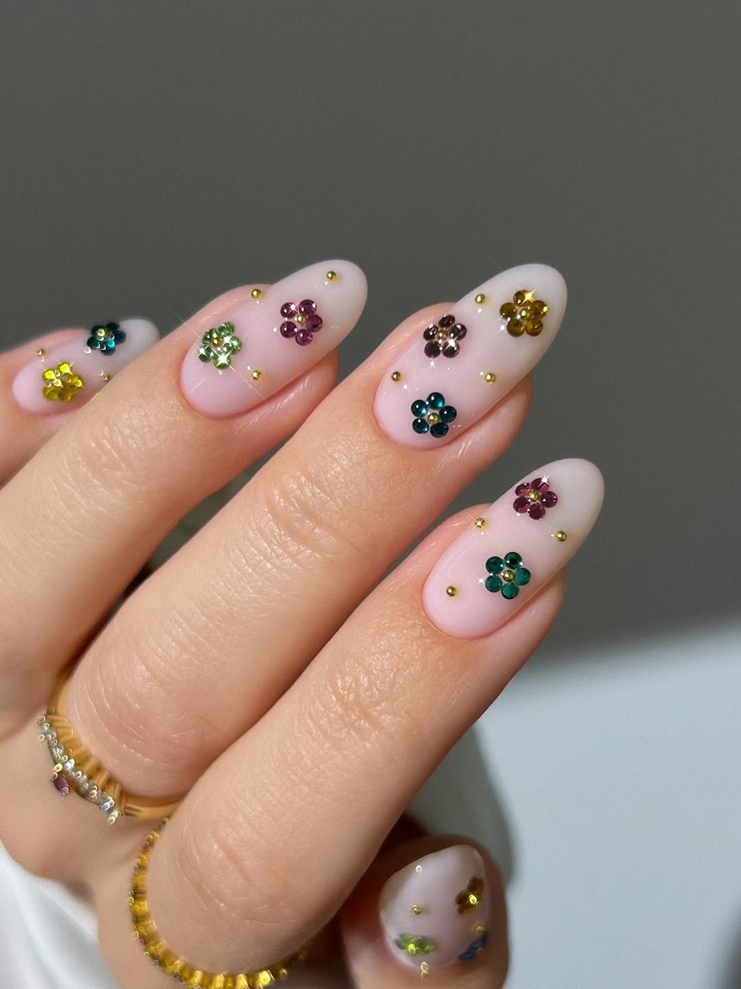 Colorful rhinestone flower nails, gem nails, spring nails, gold nails, stud nails, festival nails, milky pink nails, Kylie Jenner nails, dainty gold ring with pink diamond, curved diamond wedding band, dainty gold eternity ring, picnic nails, strawberry nails, daisy nails, yellow pink white nails, checkered nails, french tip nails, nude nails, curved multicolored eternity ring, gold ribbed ring, colorful glass nails with colorful chrome French tips and polka dots, blue pink mint green lavender cat eye, orange blue purple chrome, silver dotted ring, silver ripe ring,