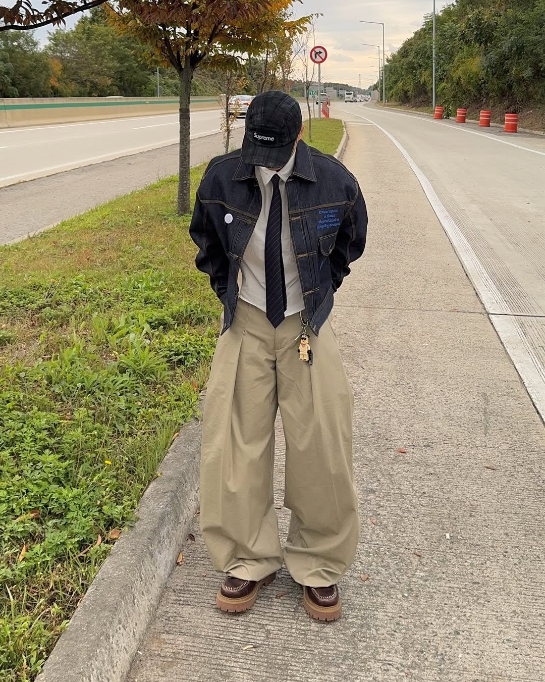 Photo shared by 황혁 on December 30, 2025 tagging @lmood_official. May be an image of wingtip shoes, overcoat, gas mask, kilt, scarecrow, road, street, curb and text.
