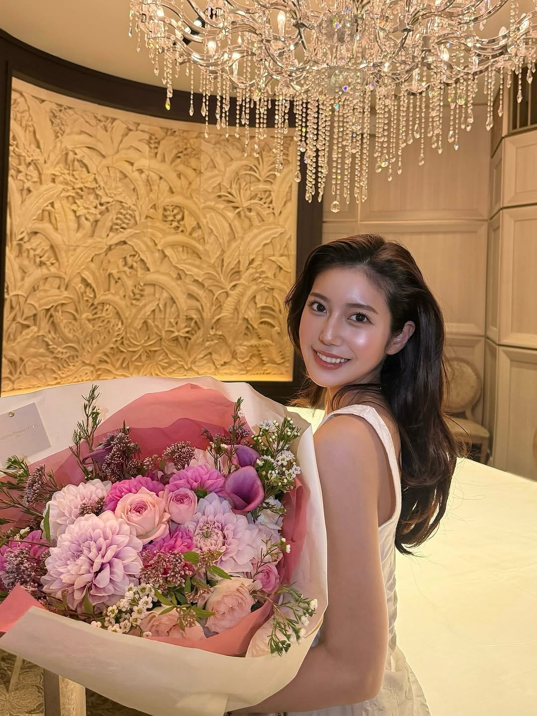 Photo by 阿部なつき on October 13, 2025. May be an image of one or more people, hair, flower arrangement, chandelier, bouquet, prairie gentian, baby's-breath, white lily, carnation, rose and text.