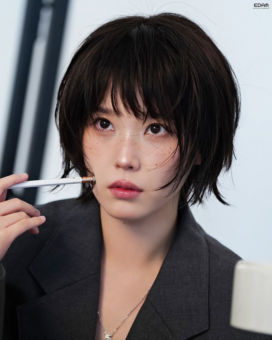 Photo shared by 아이유(IU) on November 16, 2025 tagging @dlwlrma. May be an image of one or more people, bangs, makeup, people smoking, duffle coat, cigarette, magazine and text that says 'EDAM EDAI'.