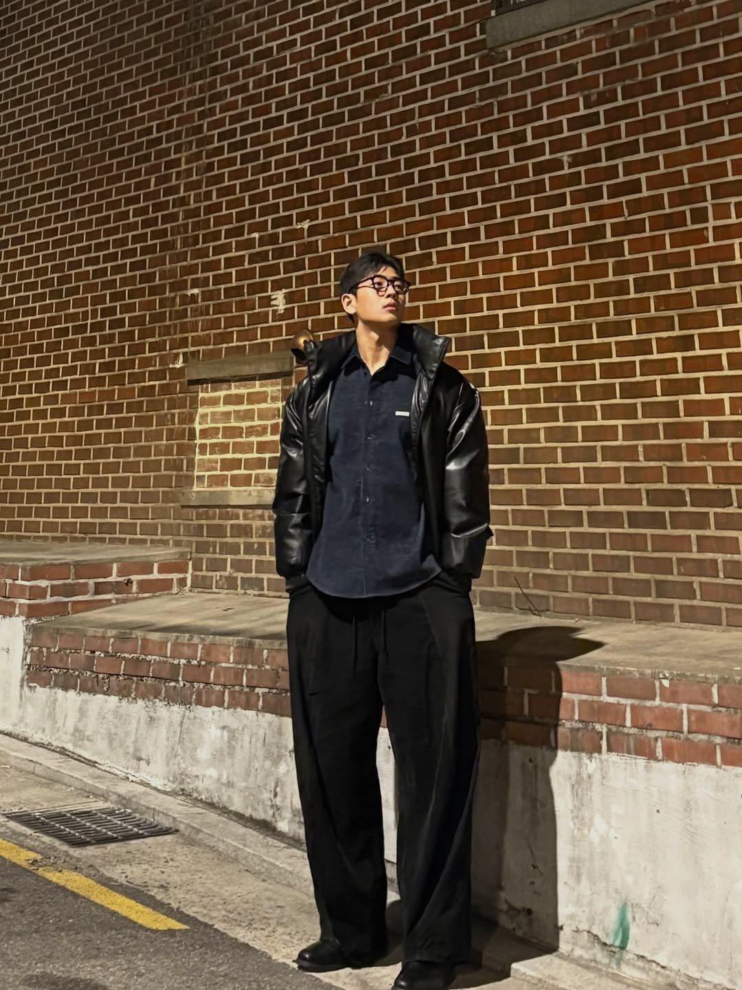 Photo shared by 이준한 on December 27, 2025 tagging @process__kr. May be an image of smoking, wingtip shoes, duffle coat, cigarette, brick wall and text.