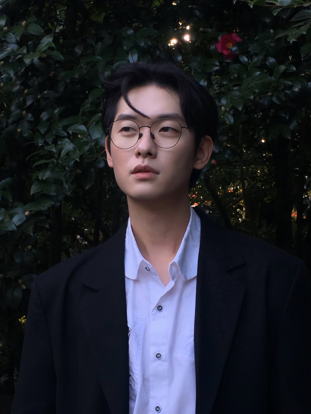 Photo shared by 백정훈 on December 05, 2025 tagging @omysunglass. May be an image of one or more people, hair, overcoat, eyeglasses, bolo tie, suit, blazer and text.