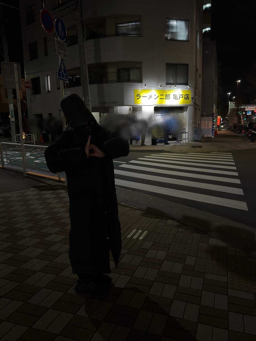 Photo by 桃乃木かな on January 07, 2026. May be an image of smoking, duffle coat, overcoat, cigarette, parka, face mask, street, night and text.