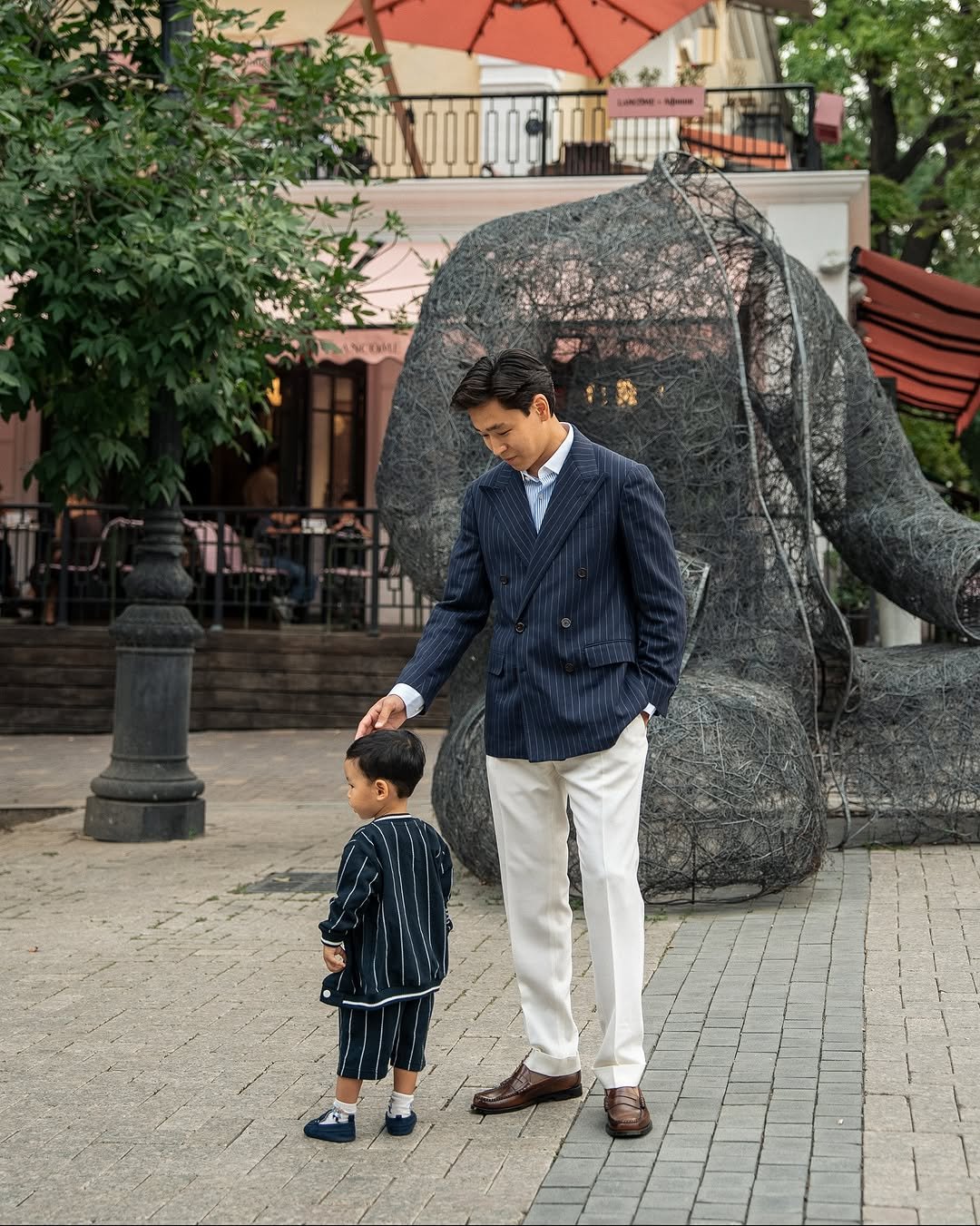 Photo by K. Beklan on August 16, 2025. May be an image of 2 people, child, people standing, elephant, suit, umbrella, parasol and text.