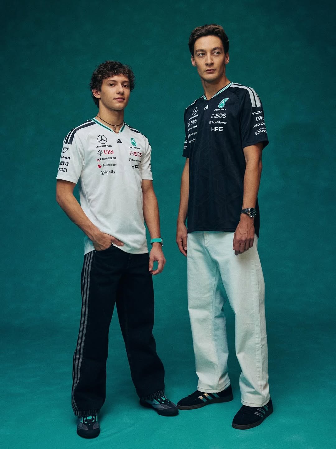 Kimi Antonelli and George Russell model our new 2026 adidas x Mercedes-AMG PETRONAS F1 Teamwear Collection. Kimi wears a white adidas driver tee, black trousers and black adidas trainers, with George in a black adidas driver tee, white trousers and black adidas trainers