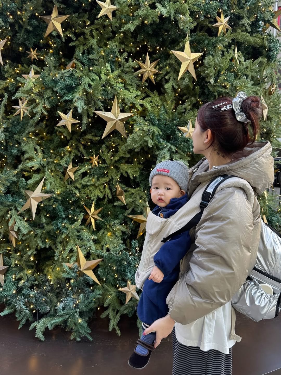 Photo by 문선우 ʚïɞ on November 25, 2025. May be an image of baby, standing, christmas tree, tinsel, sling and text.