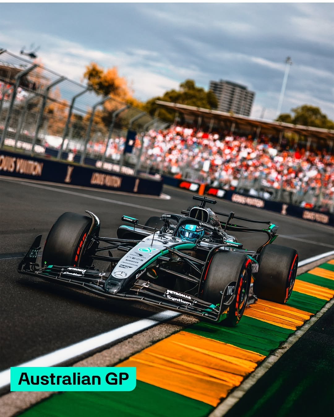 A photograph of the Mercedes W16 Formula 1 car driving on a track in daylight with crowded grandstands in the background. The text label reads "Australian GP."