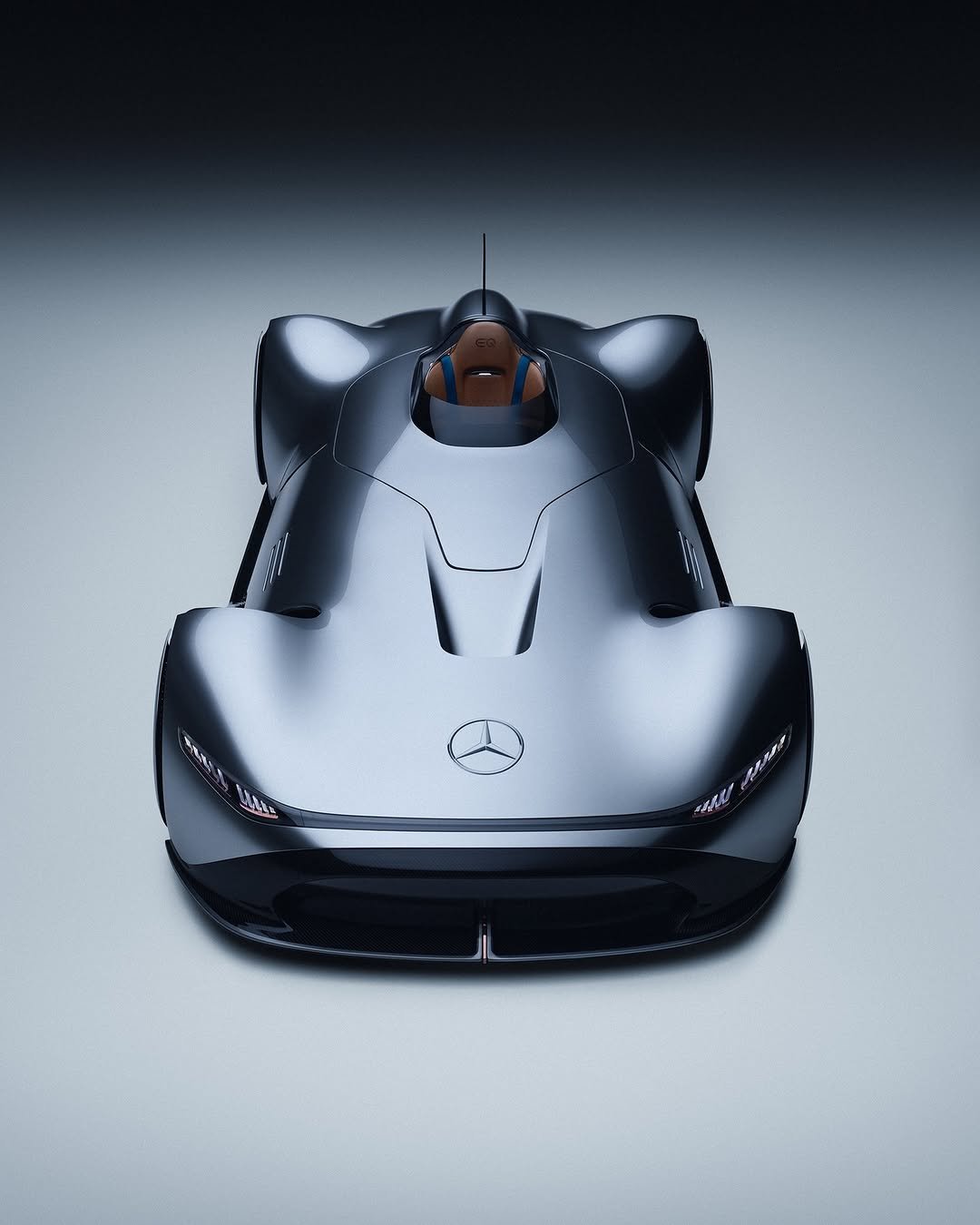 Sleek, dark metallic gray concept car, viewed from above, showcasing its futuristic design. The Mercedes-Benz logo is prominent on the hood. It features a single cockpit with a brown seat and blue straps, with "EQ" embossed. Thin, integrated headlights are visible.