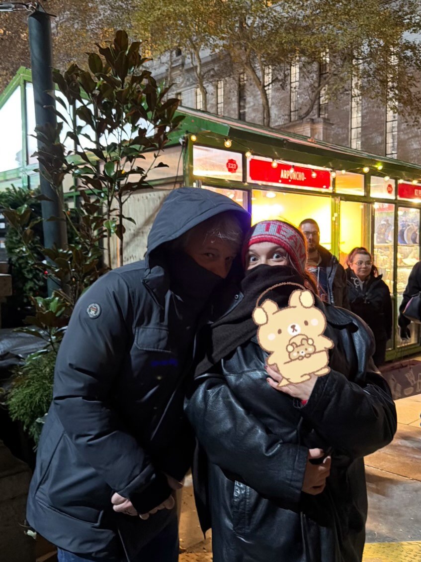 Photo by Millie Bobby Brown on December 03, 2025. May be an image of one or more people, people standing, duffle coat, parka, snowsuit, face mask and text.