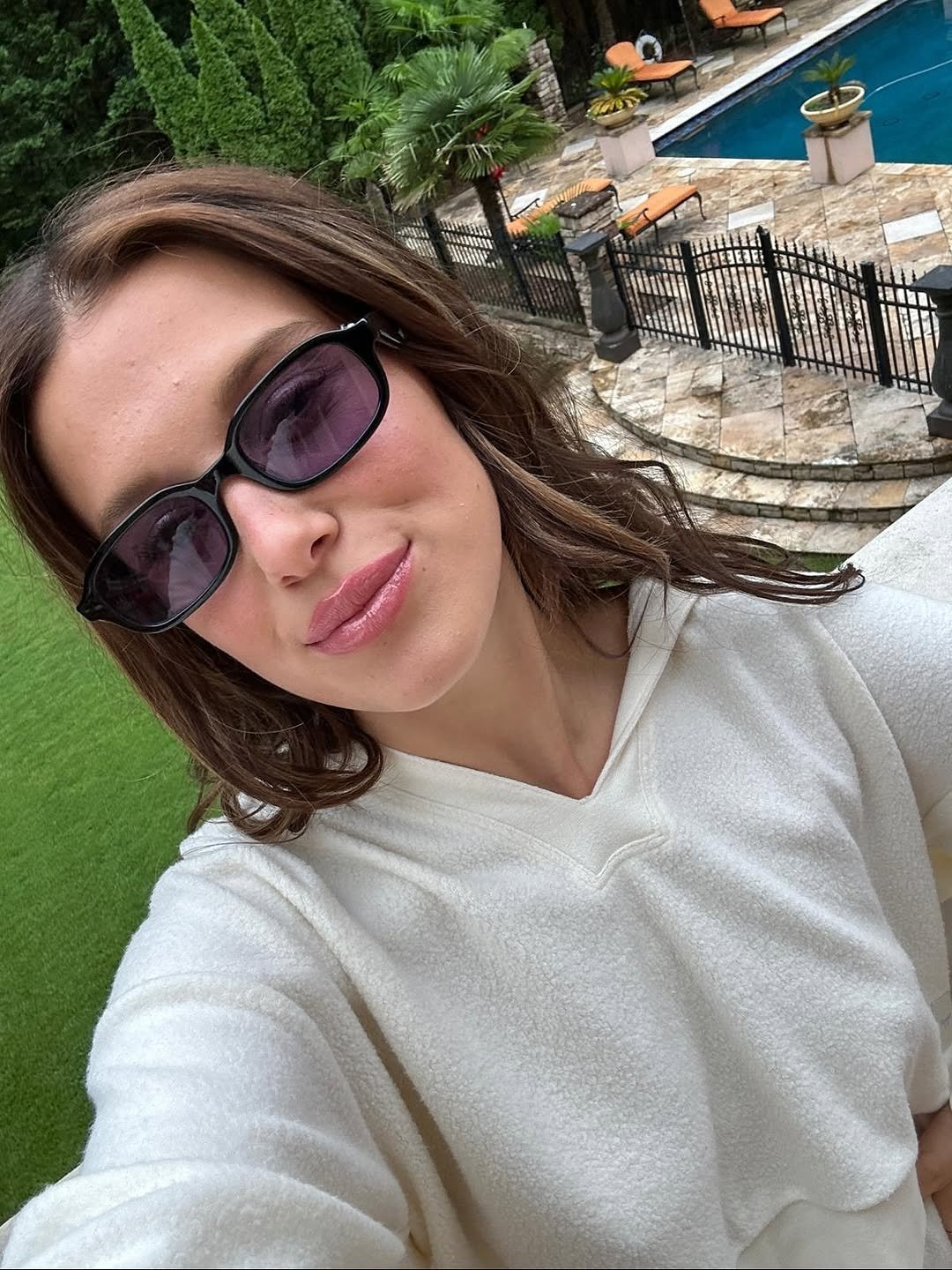 Photo shared by Millie Bobby Brown on August 15, 2025 tagging @nordstrom. May be a selfie of 1 person, bath robe, sweatshirt, sunglasses, pool and text.