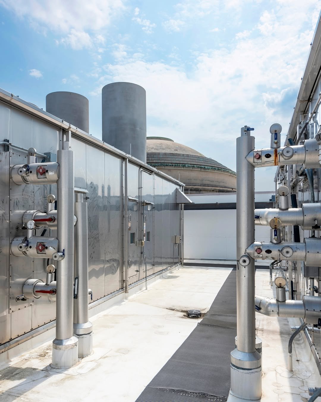 View of the Dome from MIT.nano rooftop with silmechanical system with large silver HVAC ducts and exhaust stacks in the foreground under a bright blue sky.