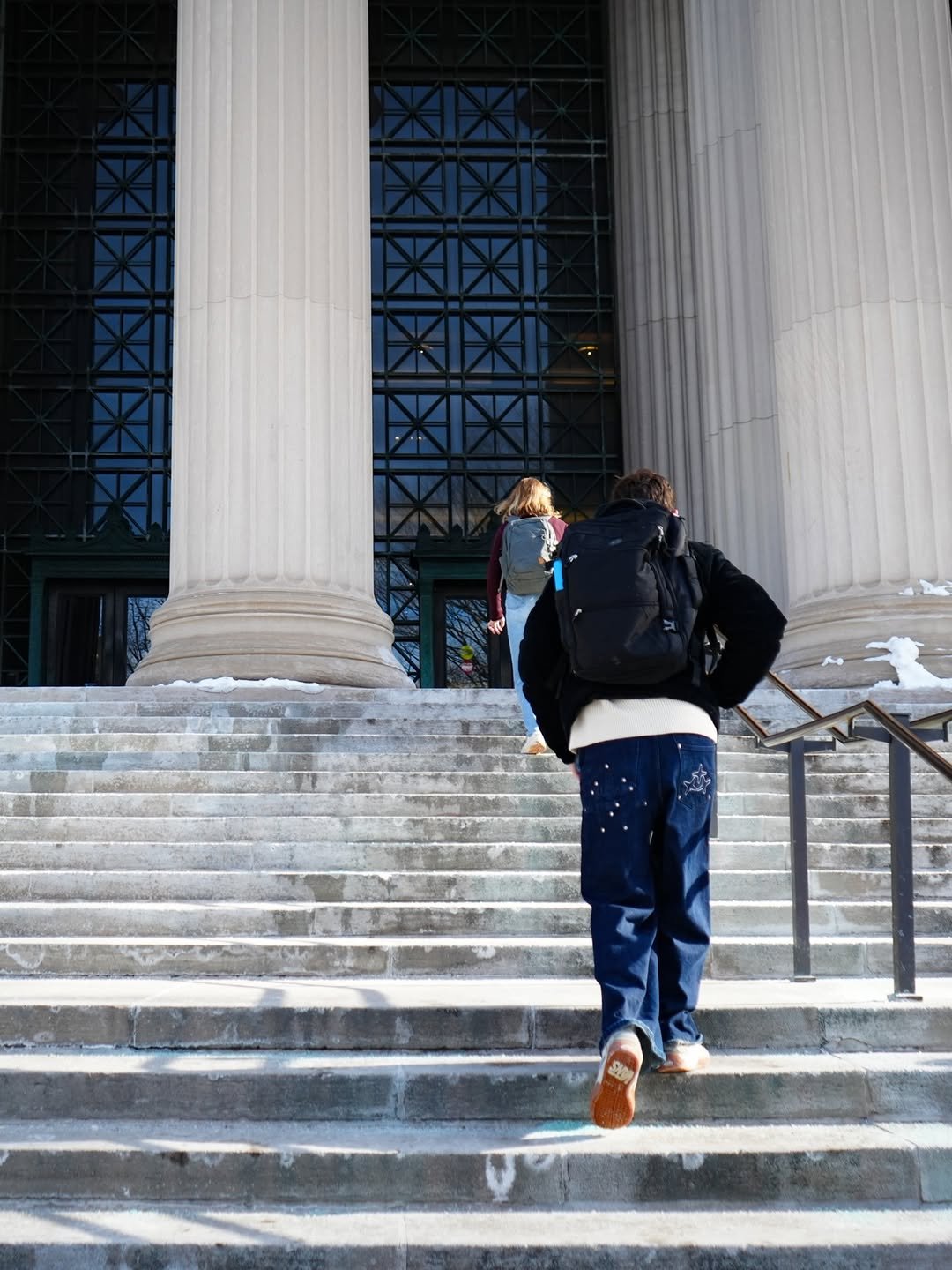 A person with a backpack walks up the concrete steps toward the entrance Building 7.