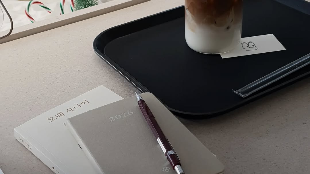 Photo by 아침서가 on January 24, 2026. May be an image of ‎studying, coffee cup, diary, coffee, pen, clipboard, desk, cornflower and ‎text that says '‎모래사나이 모 래 사나이 사나이 모래 F 2026 2026 ه‎'‎‎.
