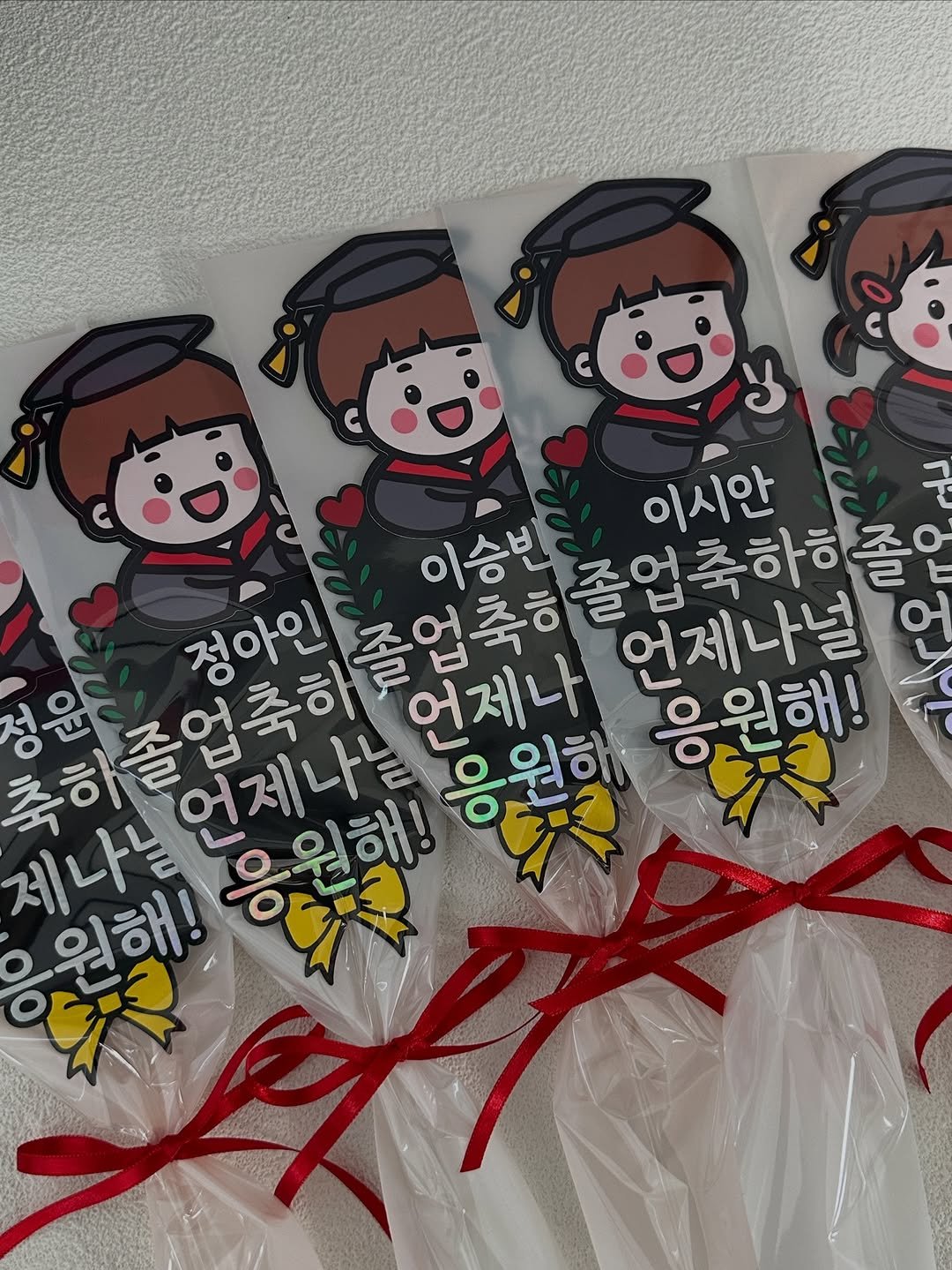 Photo by 밝음토퍼 | 토퍼창업•토퍼클래스•토퍼제작 전문점 on February 18, 2026. May be an image of lollipop and text that says 'y 구 이승빈 이시안 정아인 졸업축하 정윤 졸업축하 언제나는 워해! % 응원해 언제나 졸업축하하줄 언제나널 축하졸 O 응원해! 제나느 OO 원해!'.
