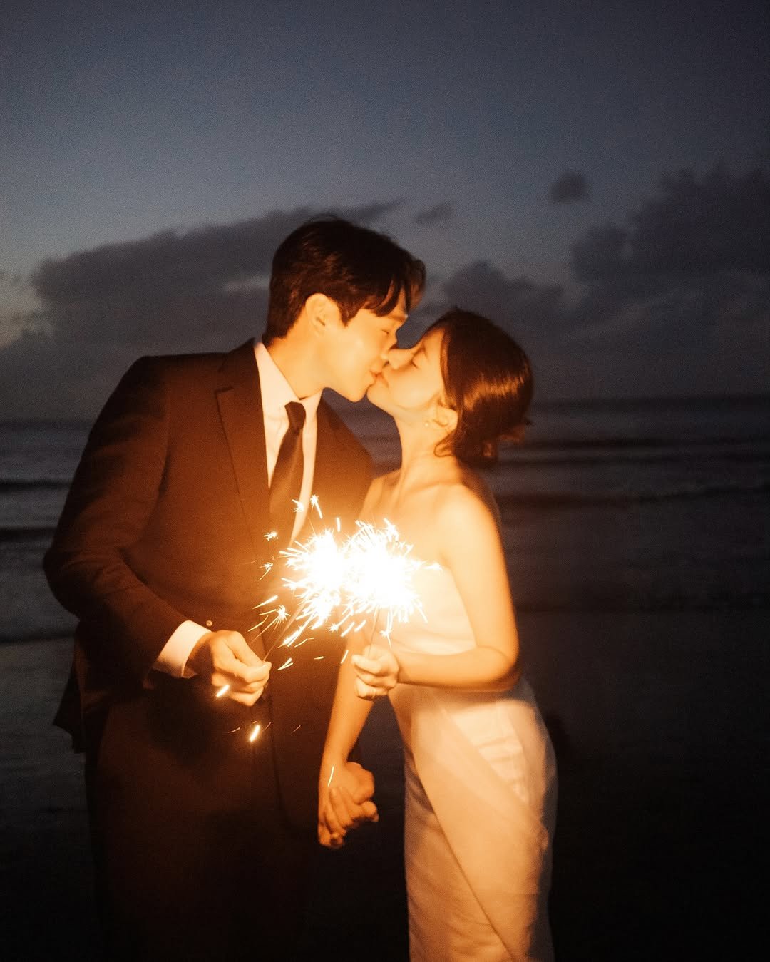 Photo shared by 온리그래퍼/ 제주스냅 서울스냅 웨딩스냅 커플스냅 on October 16, 2025 tagging @by_moon_official, @by_moon_stylist_suji, and @only.grapher_wedding. May be an image of people kissing, sparkler, fireworks, wedding and text.