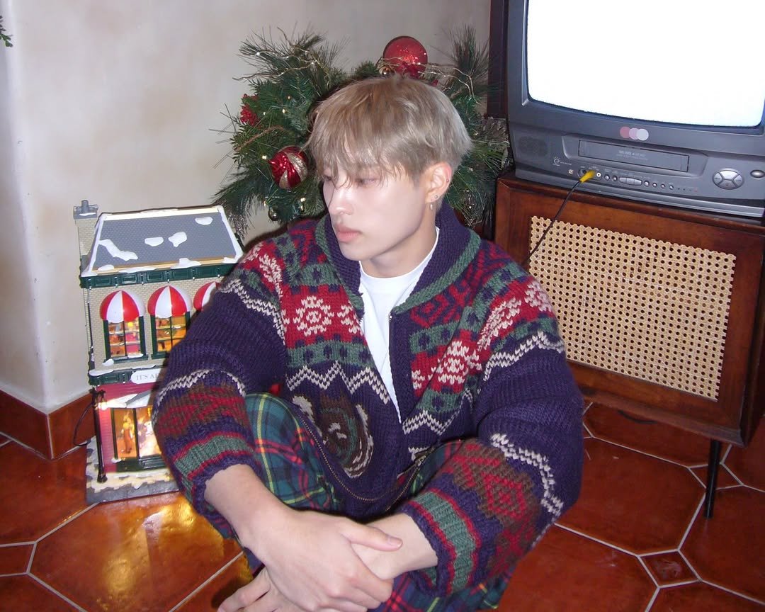 Photo by P1Harmony (피원하모니) on December 24, 2025. May be an image of one or more people, blonde hair, bangs, sweater, portable cassette player, turtleneck, cardigan, bath robe, tinsel, knit and text.